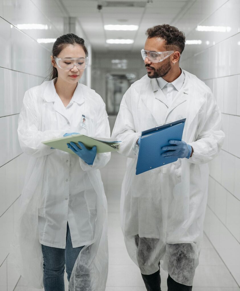 Two scientists in lab coats discussing research documents in a laboratory hallway.